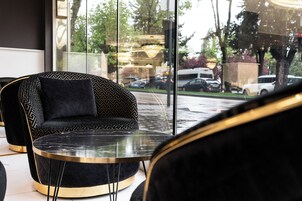 Un interior moderno con un sofá tapizado en negro y una mesa de vidrio, amplias ventanas con vistas a coches aparcados y árboles.