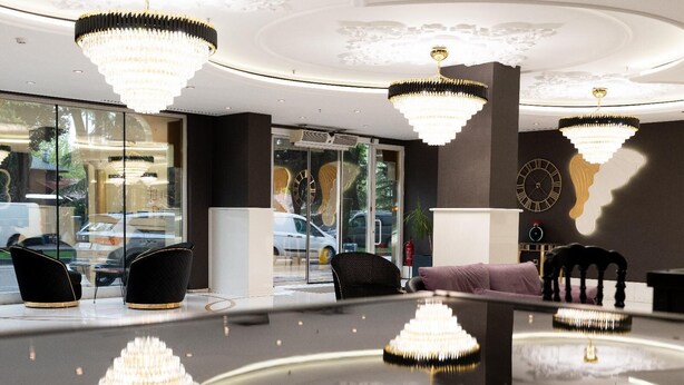 Un vestíbulo moderno con múltiples candelabros, una zona de estar con sofás y sillones, y grandes ventanales con vistas a la calle.