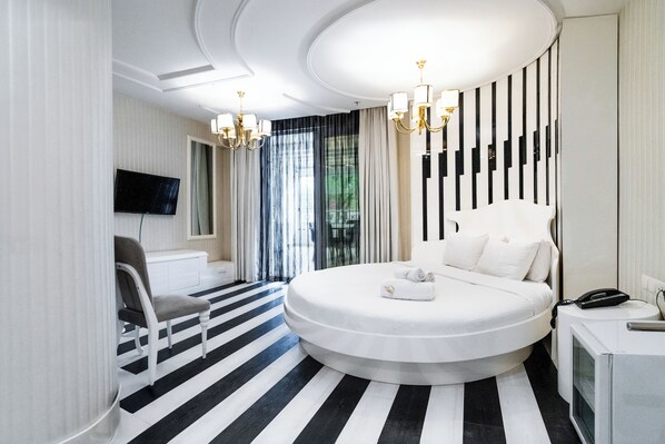 A modern hotel room with a round bed, a TV mounted on the wall, a desk with a phone, and a chair. - GOLDEN PARS HOTEL (Bursa)