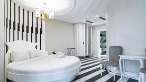 Un dormitorio moderno con una cama redonda, un sillón gris, una mesita y una araña.