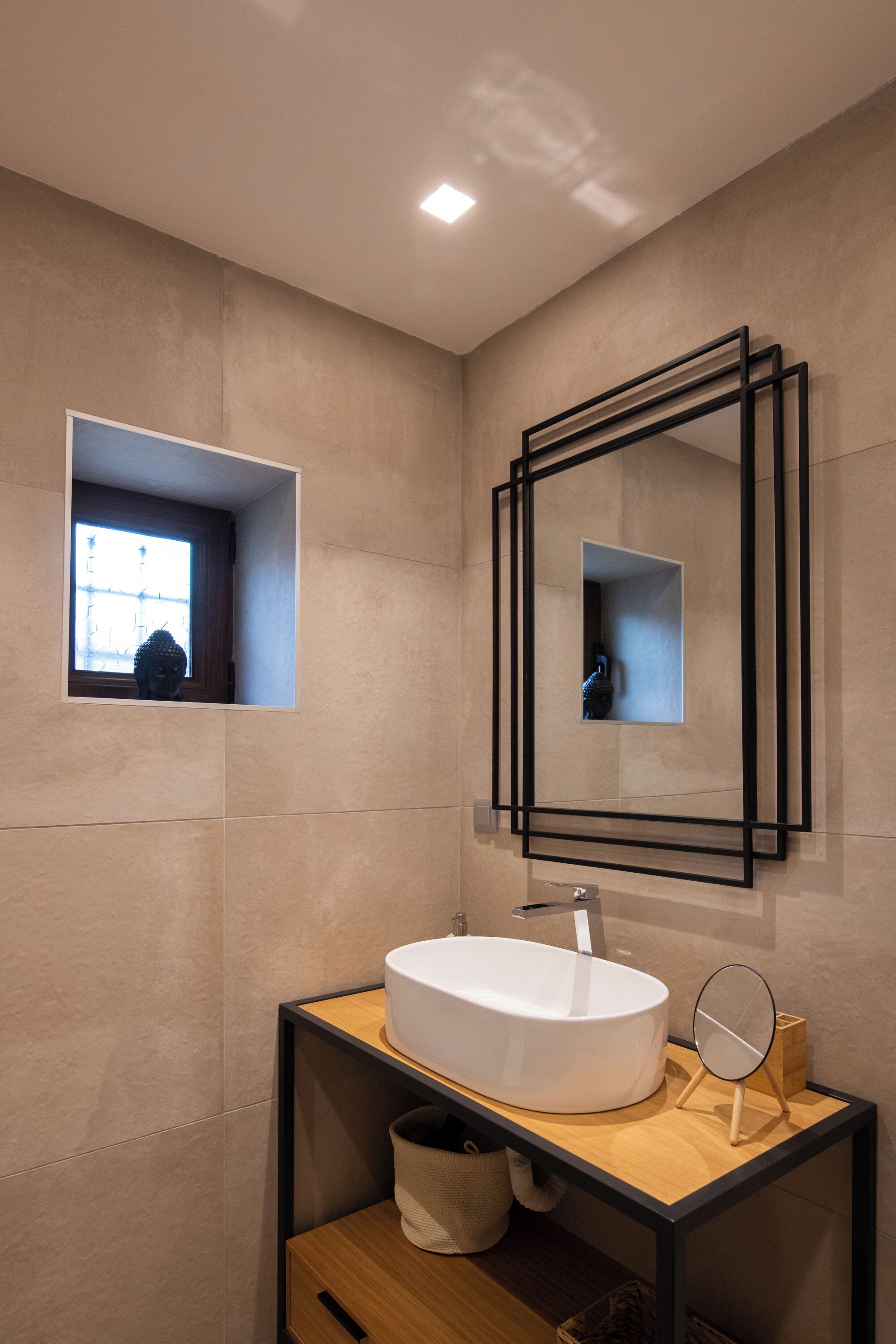 A modern bathroom with a large rectangular mirror, a white sink, and a small window.