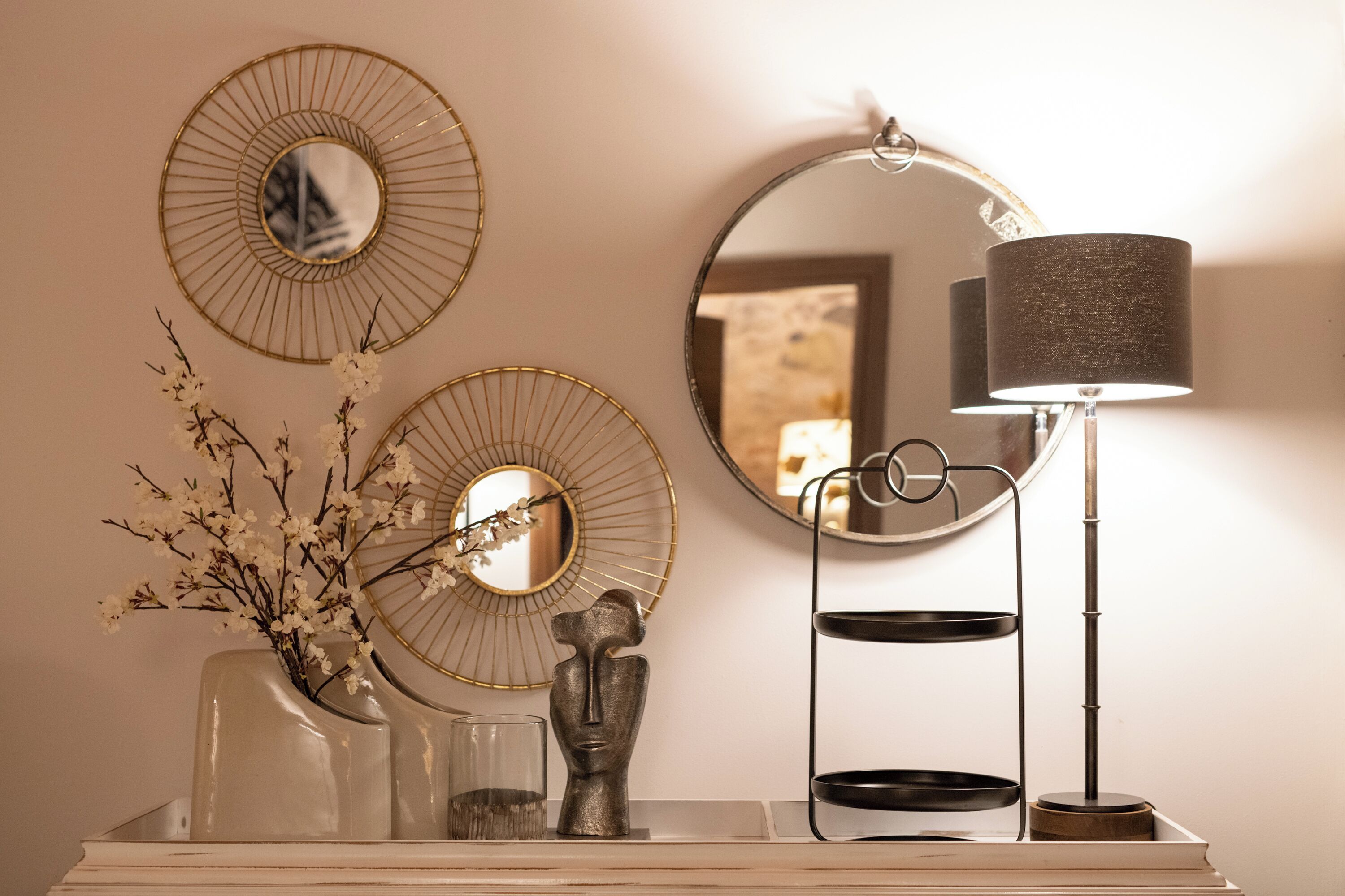 A vanity with a mirror, decorative plates, a vase with flowers, a sculpture, and a lamp.