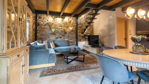 Una sala de estar moderna con una pared de piedra, un sofá azul, una mesa de centro y una zona de comedor con una mesa redonda.