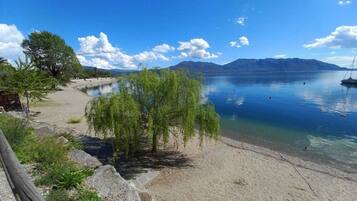 A lakeside view with a sandy beach, trees, and mountains in the background.