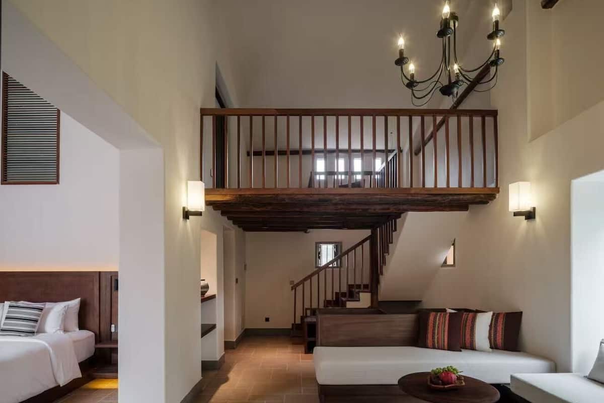 A spacious living area with a high ceiling, a wooden staircase, and a chandelier.