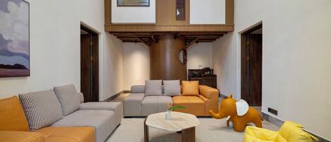 A spacious living area with a high ceiling, a central wooden column, and a view of a kitchen area.
