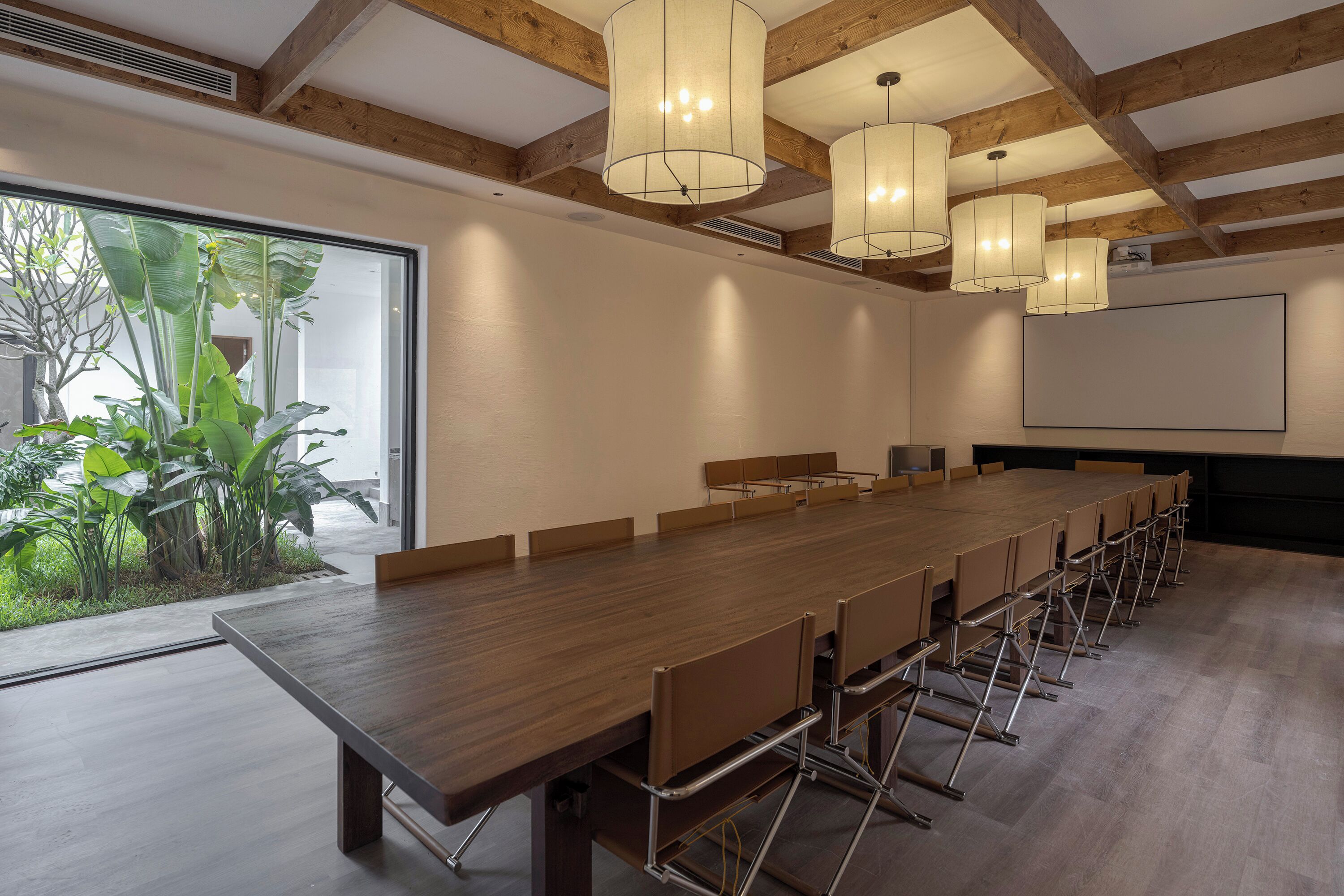 A conference room with a long wooden table, metal chairs, and pendant lights.