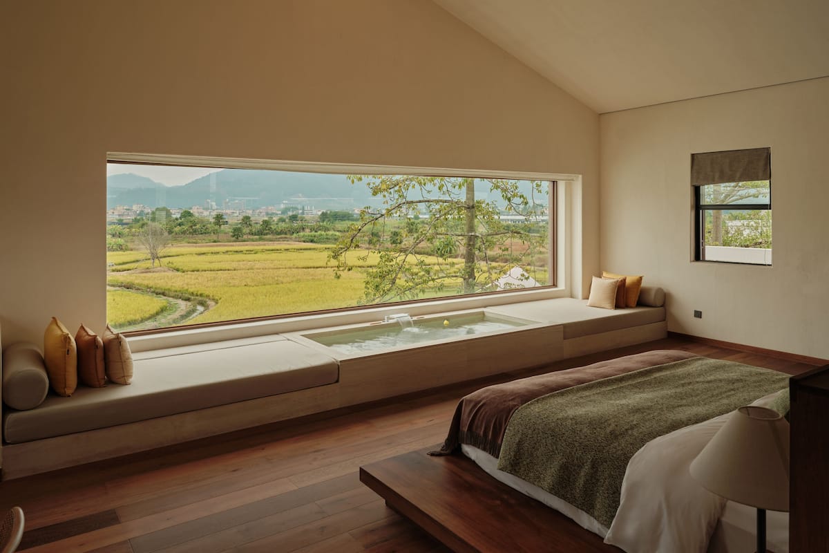A bedroom with a large window, a built-in bathtub, and a view of a green landscape.