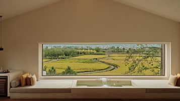 Una habitación con un ventanal grande con vistas a un campo de arroz, un banco empotrado con cojines y una pequeña fuente.