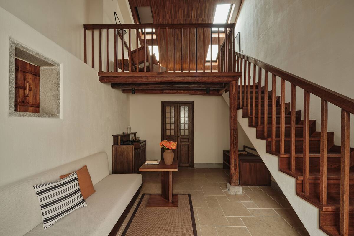 A spacious living area with a wooden staircase, a sofa, a small table with a vase, and a door with a window above it.