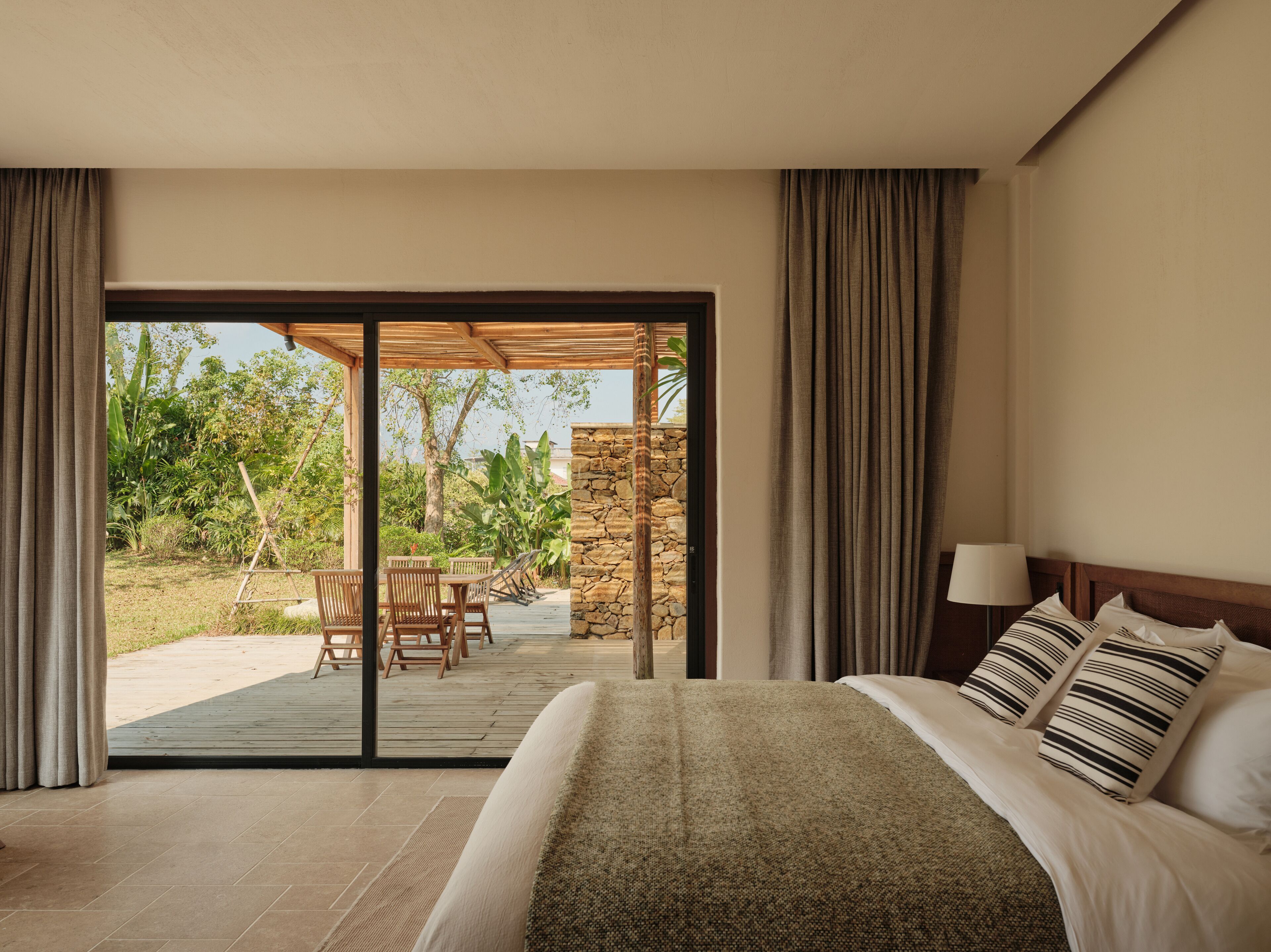 A bedroom with a large bed, a wooden headboard, and a view of an outdoor patio with a table and chairs.