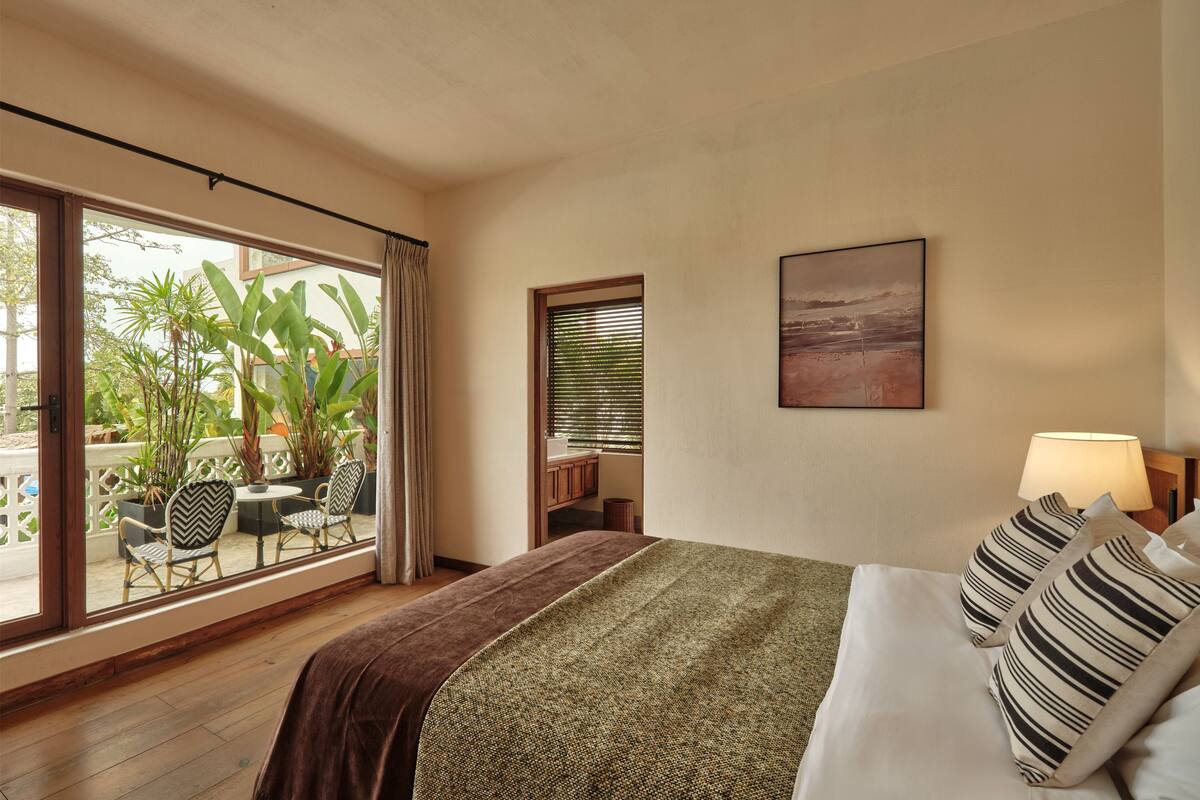 A hotel room with a large bed, a view of the outdoor area, and a painting on the wall.