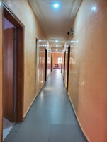 Um corredor comprido e estreito com portas de madeira à esquerda e chão de azulejos.