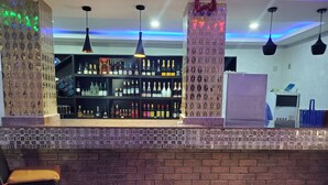 Eine Bar mit einer gefliesten Theke, Regalen voller Spirituosenflaschen, hängenden Pendelleuchten und einer Ziegelwand.