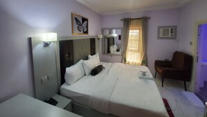 Ein Hotelzimmer mit Bett, Stuhl, Schreibtisch, Spiegel, Deckenventilator und einem Fenster mit Vorhängen.