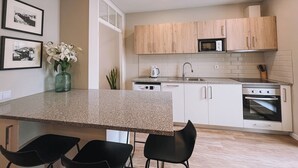 A modern kitchen with a granite countertop, white cabinets, a microwave, and a stove. There are two black chairs at the island and a vase with flowers.
