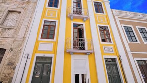 A multi-story building with a yellow facade, white trim, and a balcony with ornate metal railings.