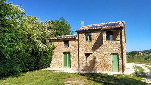 A stone building with green doors and a tiled roof, surrounded by greenery.