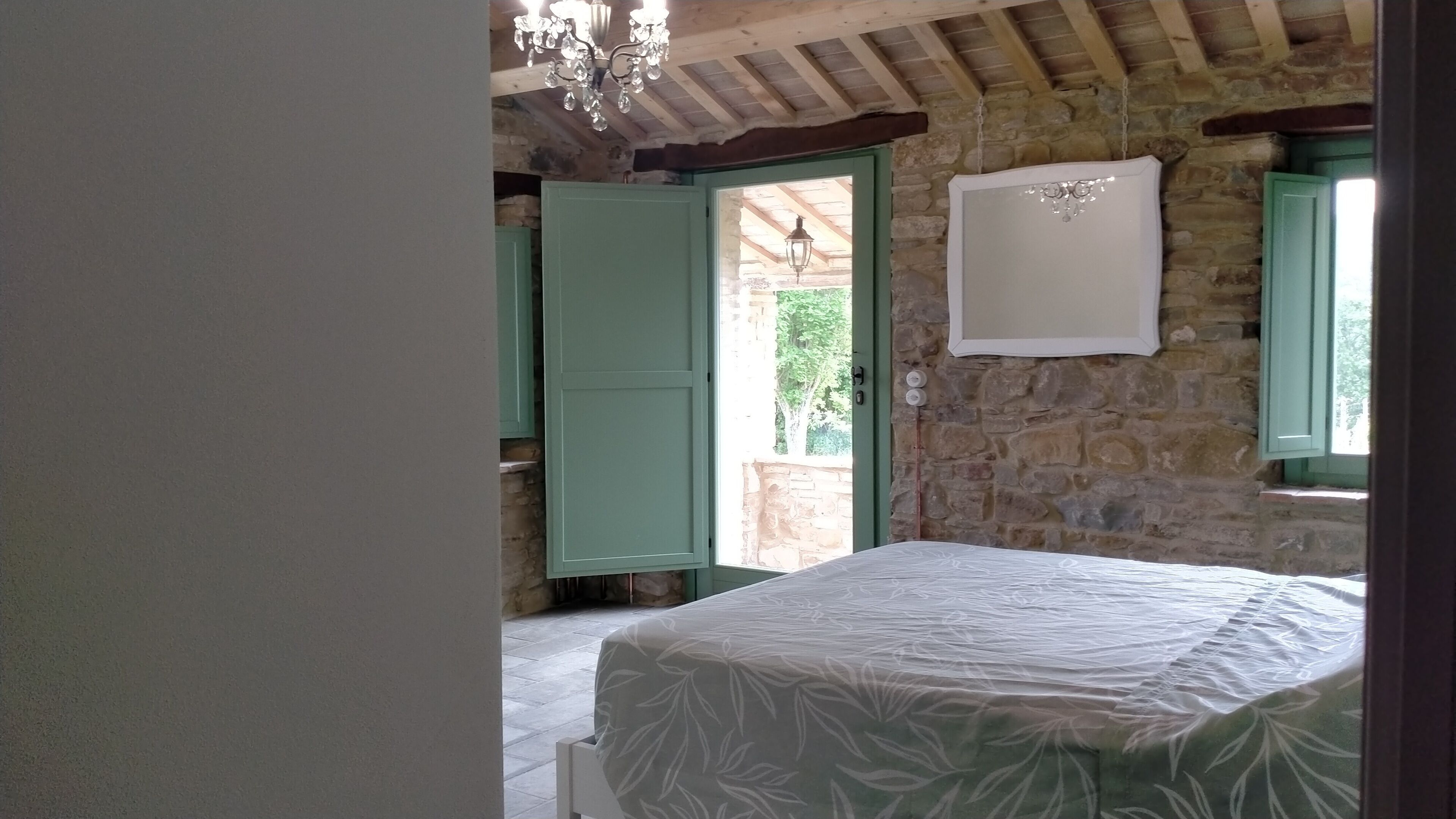 A bedroom with a bed, a stone wall, and a window with green shutters.