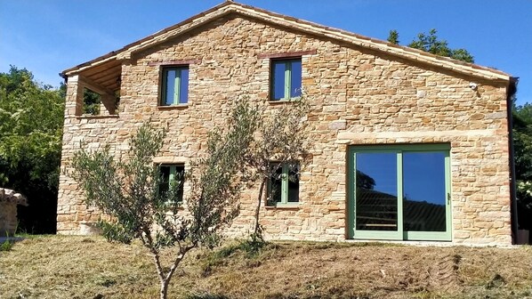 A stone house with two windows and a large sliding glass door.