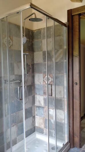 A glass-enclosed shower with a handheld showerhead and a wall-mounted faucet.