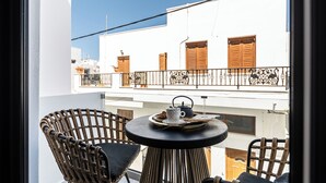 A balcony with wicker chairs, a table with a teapot and cup, and a view of white buildings with wooden shutters. - V Luxury Apartments Naxos (Naxos)
