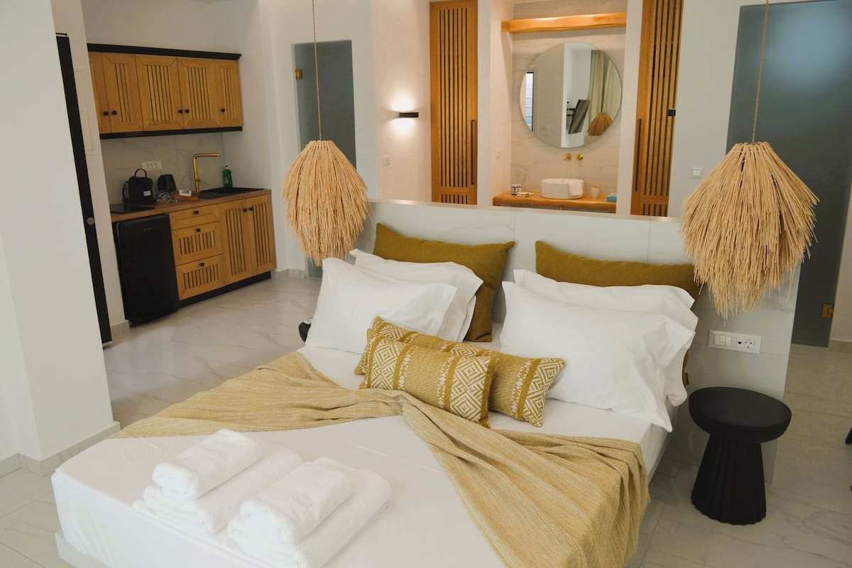 Habitación de hotel con cama, mesita de noche, taburete pequeño, lavamanos y espejo.