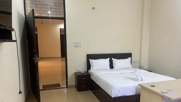Ein Hotelzimmer mit einem Bett, Nachttischen, einem Schreibtisch und einer Tür, die zu einem Flur führt.