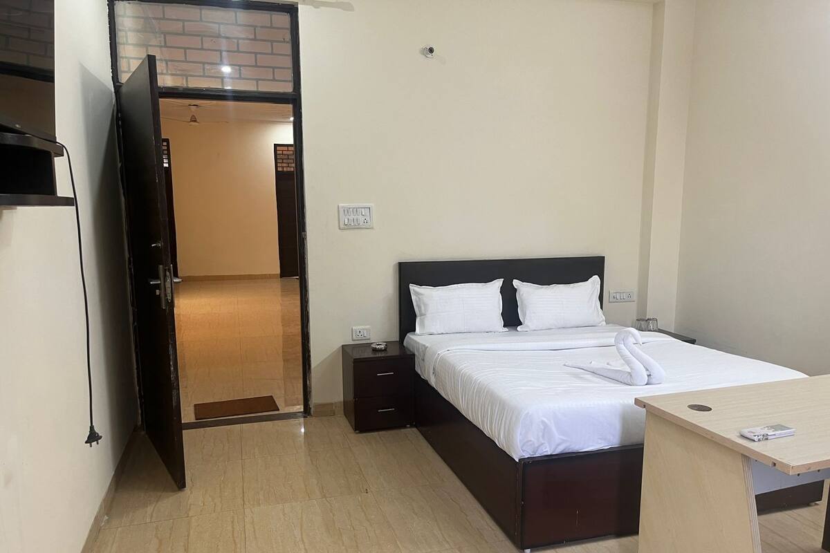 Ein Hotelzimmer mit einem Bett, Nachttischen, einem Schreibtisch und einer Tür, die zu einem Flur führt.