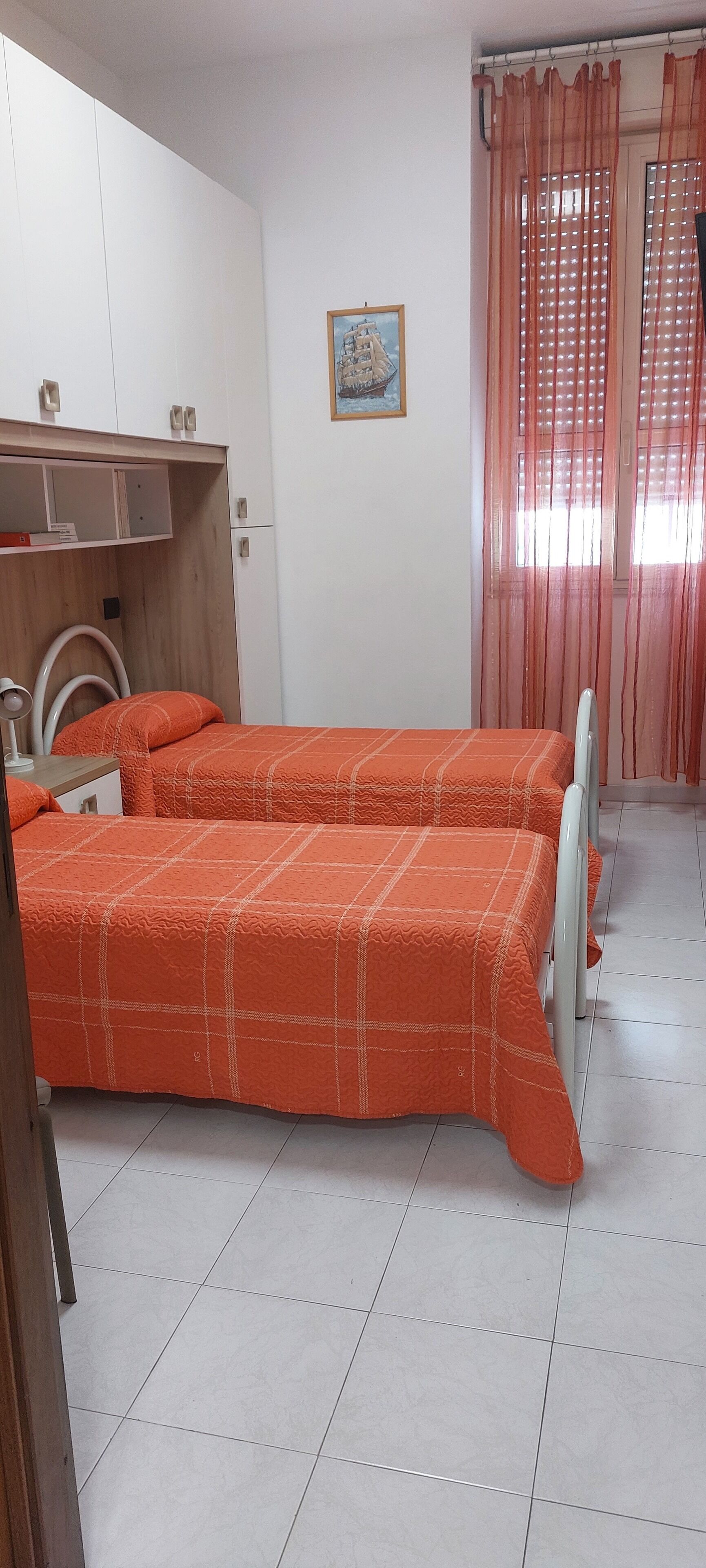 A bedroom with two beds, a wooden wardrobe, a small table, and a window with curtains.