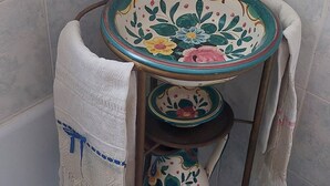 Une petite salle de bain d’angle avec une petite table ronde ornée de motifs floraux, une serviette blanche accrochée au mur et des toilettes.