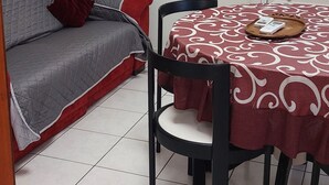 Une pièce avec un canapé gris, une table à manger recouverte d’une nappe rouge et un meuble blanc aux portes en verre.