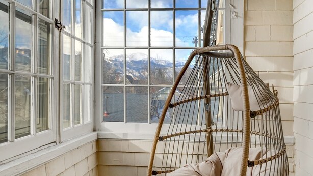 A room with a large window, a wicker hanging chair, and a view of snow-capped mountains. - Noble Summit BBQ & Fire Pit  & Scenic Views (Colorado Springs)