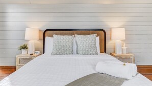 A neatly made bed with a white quilt, two patterned pillows, and a white throw blanket. There are two bedside lamps with white shades and a small bedside table with a plant and a clock. - Noble Summit BBQ & Fire Pit  & Scenic Views (Colorado Springs)