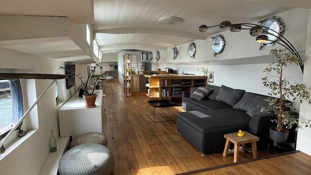 A spacious living area with a wooden floor, a dark sofa, a small table, and a potted plant.