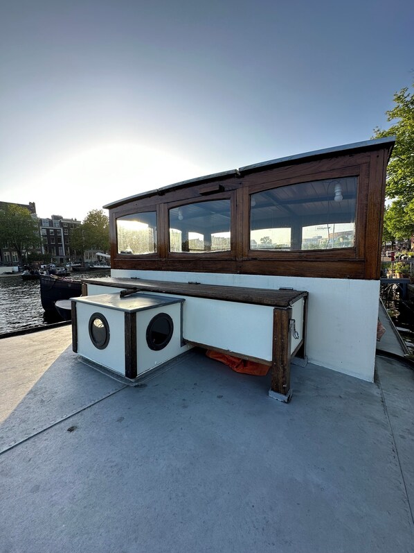 A wooden structure with large windows overlooking a canal, featuring a bench and a small table.