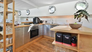A modern kitchen with wooden shelves, stainless steel appliances, and a potted plant.