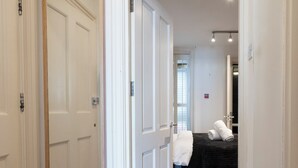 Un couloir avec un plancher en bois, des portes blanches et, au fond, un lit doté d’une tête de lit noire.
