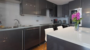 Une cuisine moderne avec des meubles de couleur sombre, un évier en acier inoxydable et un plan de travail blanc.