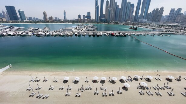 A marina with boats docked, a sandy beach with umbrellas, and a city skyline in the background. - Marina Vista Emaar Beachfront Apartments (Dubai)
