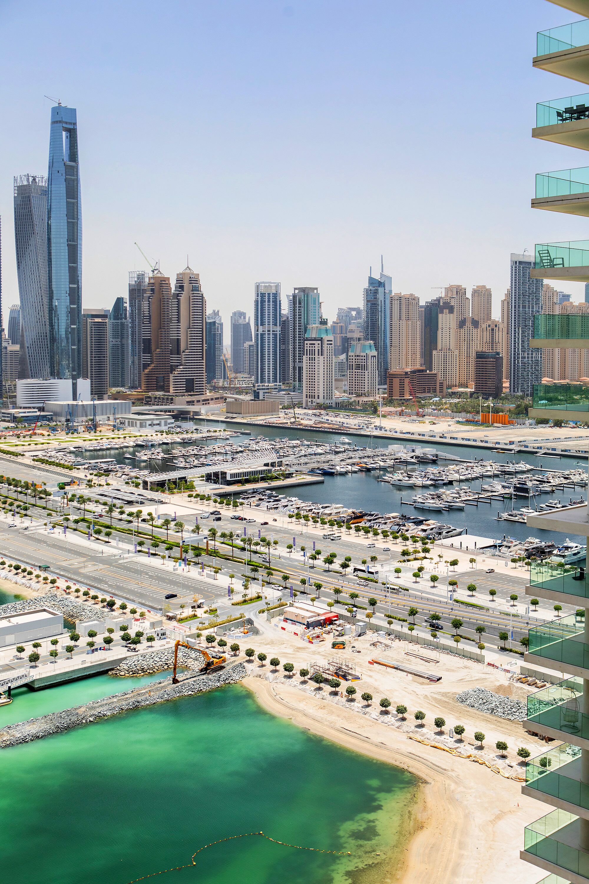 A marina with boats, a beach, and a city skyline with modern buildings.