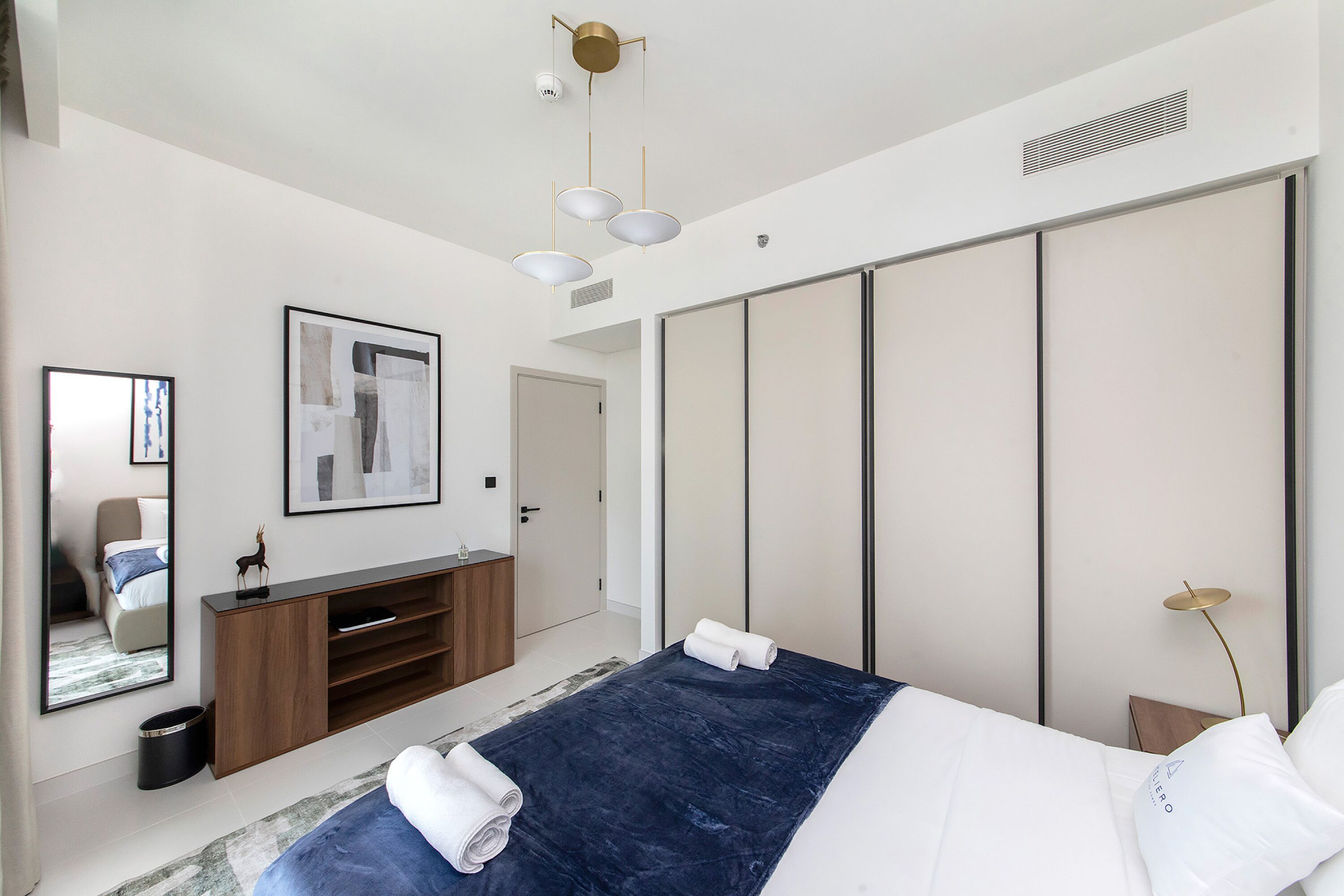 Ein modernes Schlafzimmer mit einem großen Bett, einem Kleiderschrank, einem Schminktisch mit Spiegel und einer Deckenleuchte.