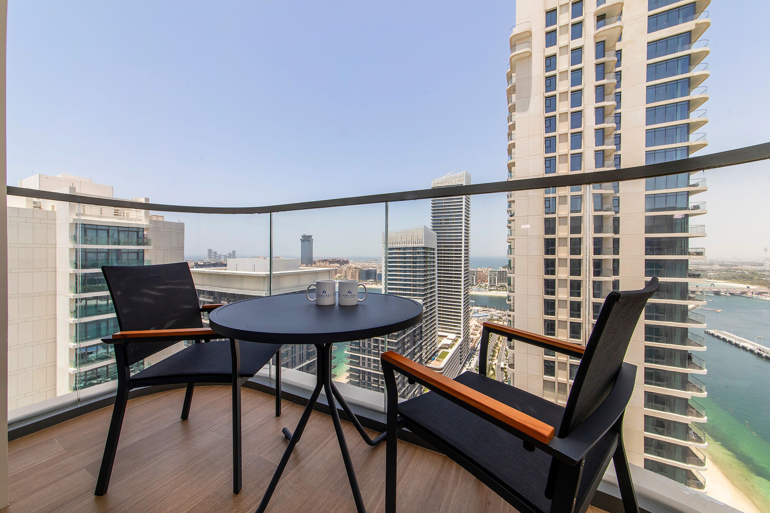 Ein Balkon mit einem runden Tisch und zwei Stühlen, der auf einen Stadtblick mit hohen Gebäuden und einem Gewässer blickt.