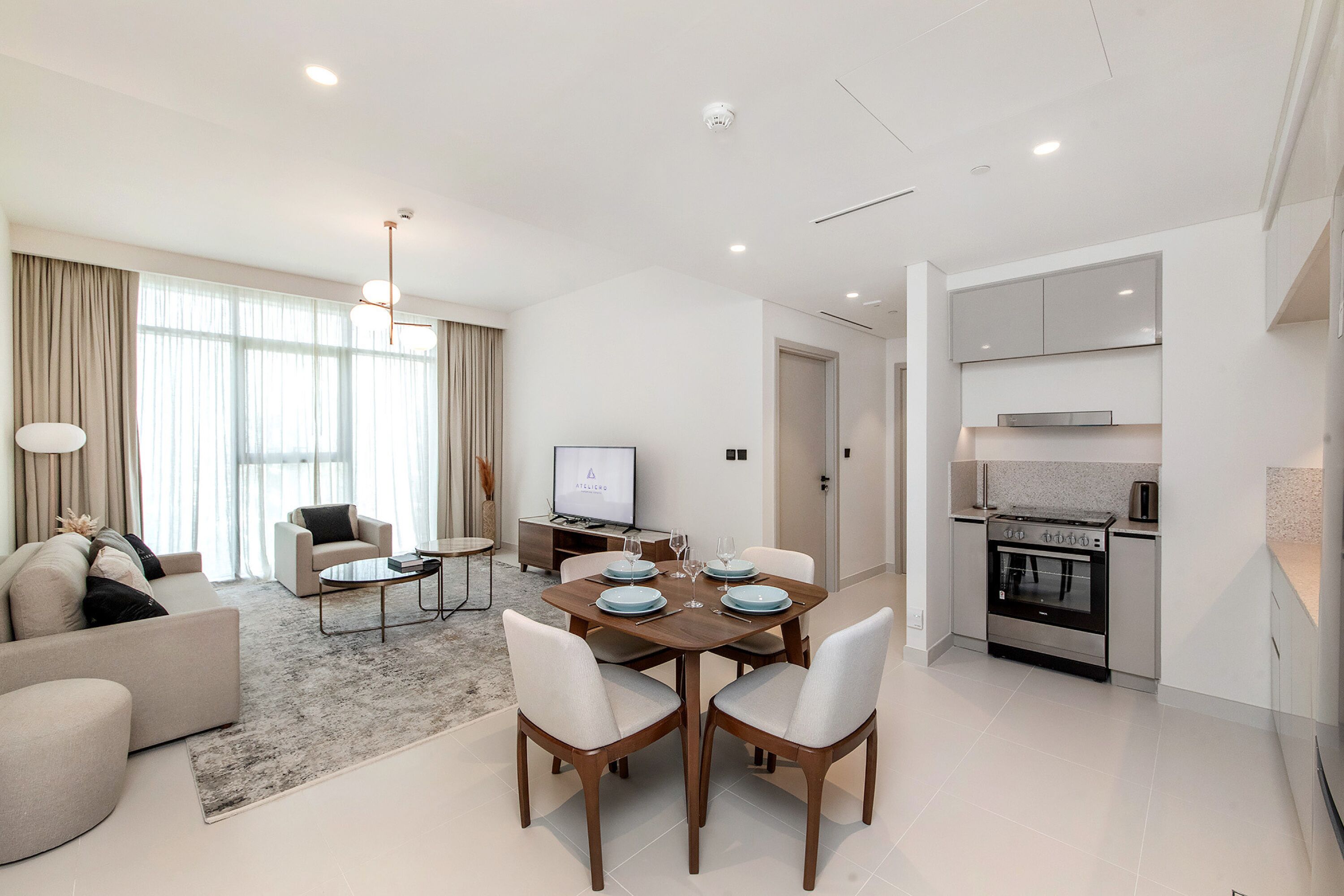 A modern living room with a dining area, a flat-screen TV, and a kitchen with a built-in oven.