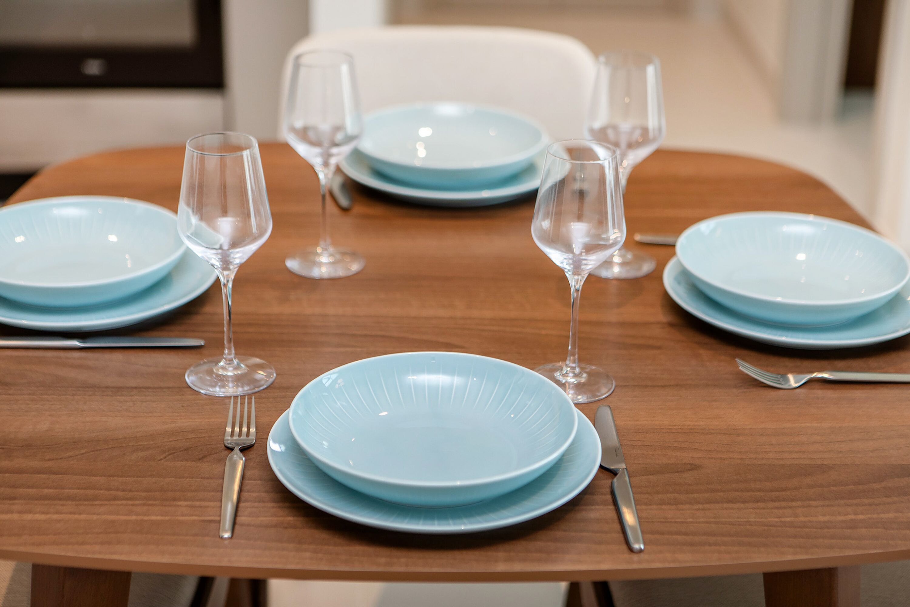 Mesa de jantar posta com pratos azuis, copos de vinho e talheres.