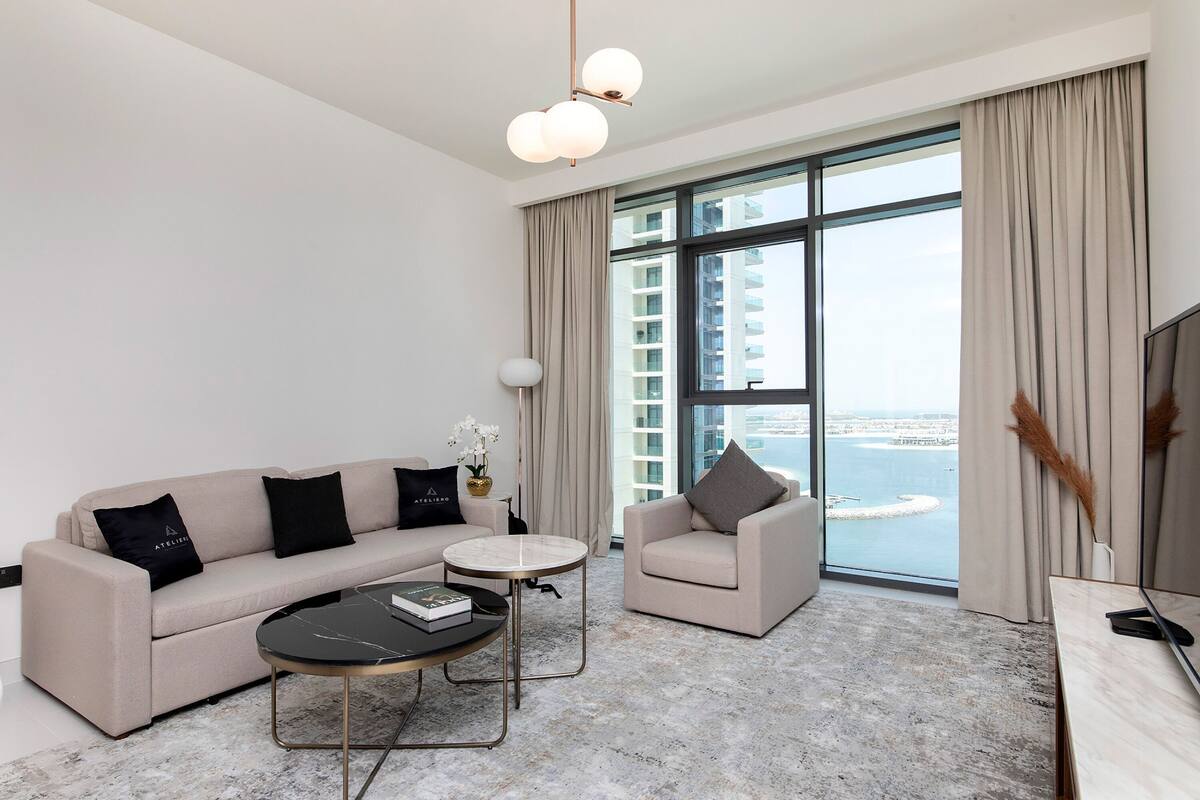 A modern living room with a sofa, armchair, coffee table, and a large window with a city view.