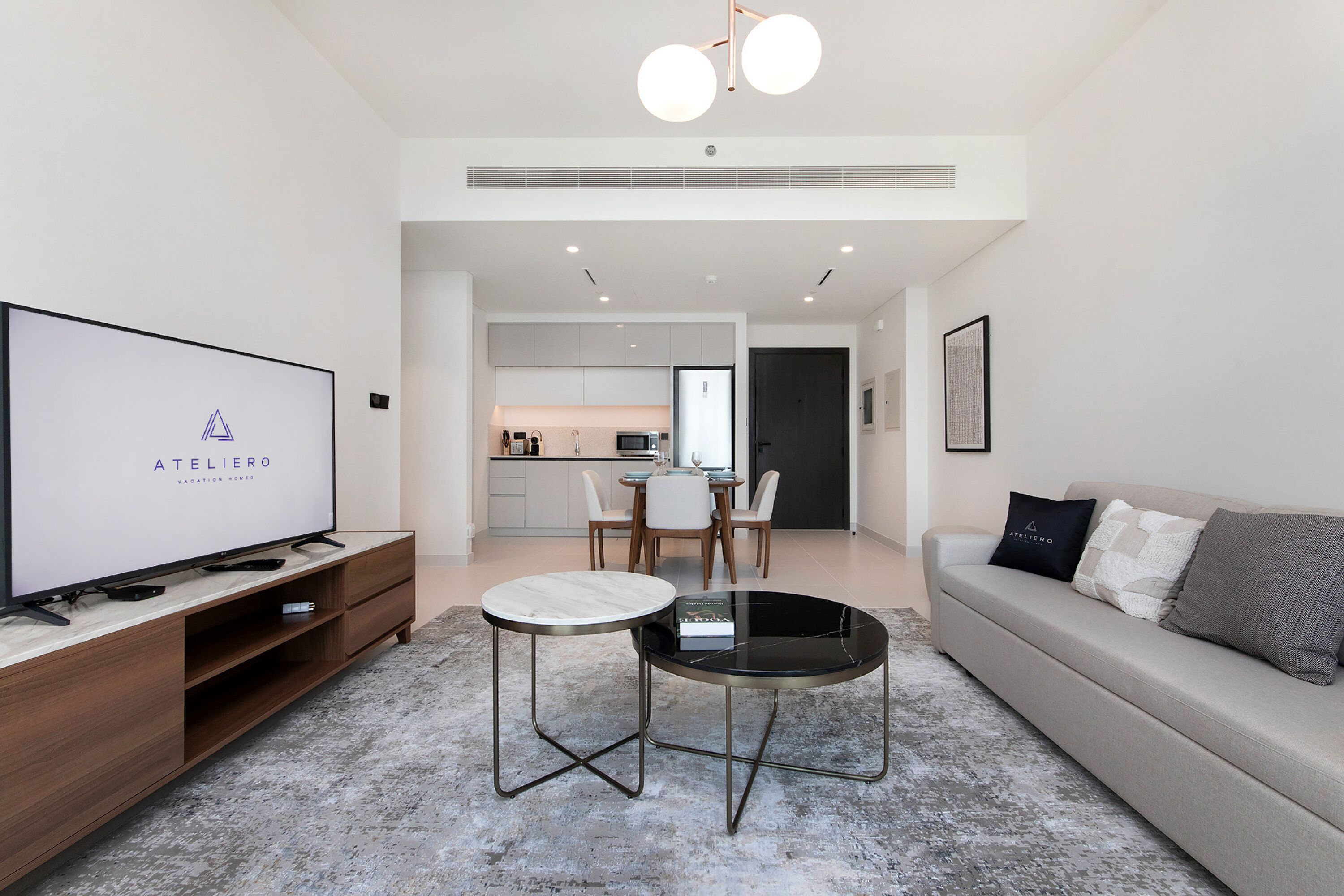 Een moderne woonkamer met een flatscreen televisie, een bank, een salontafel en een eethoek op de achtergrond.