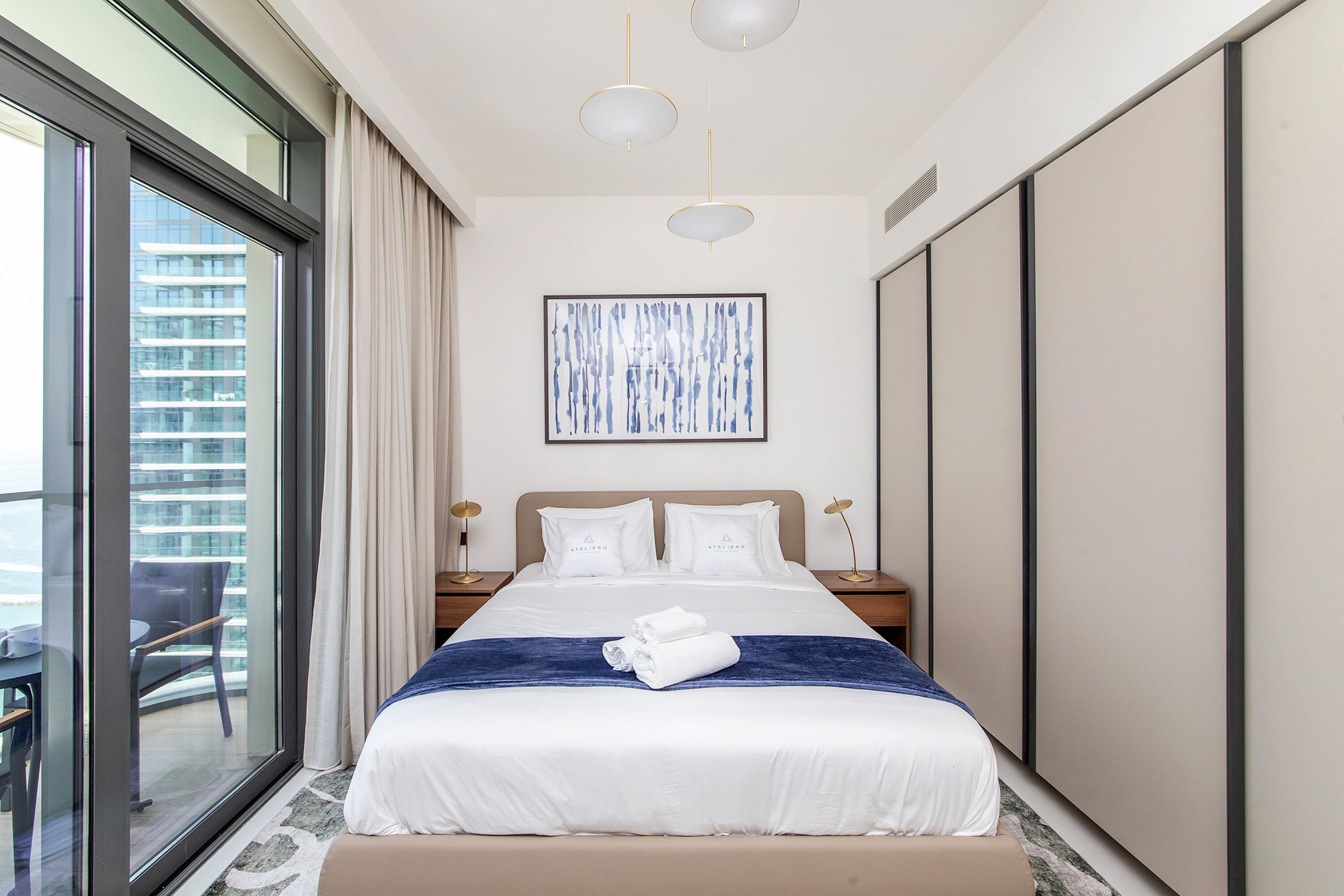 A hotel room with a large bed, a view of a cityscape, and a balcony with a table and chair.