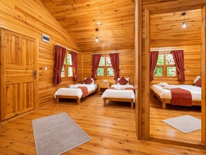 Uma cabana de madeira com três quartos, cada um com uma cama, uma mesa de cabeceira e uma janela com cortinas.