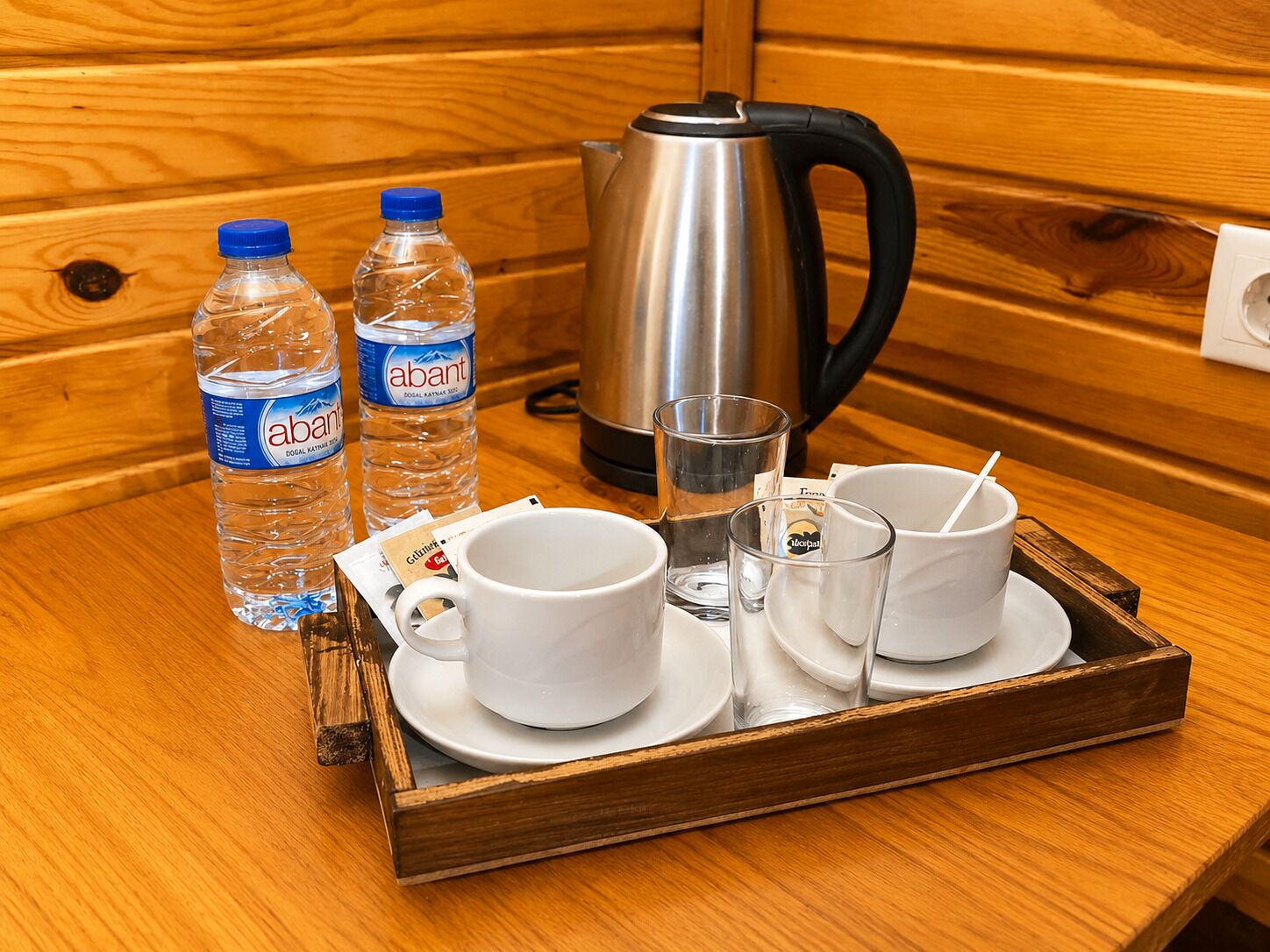 A wooden tray with a kettle, two water bottles, and four cups with saucers.